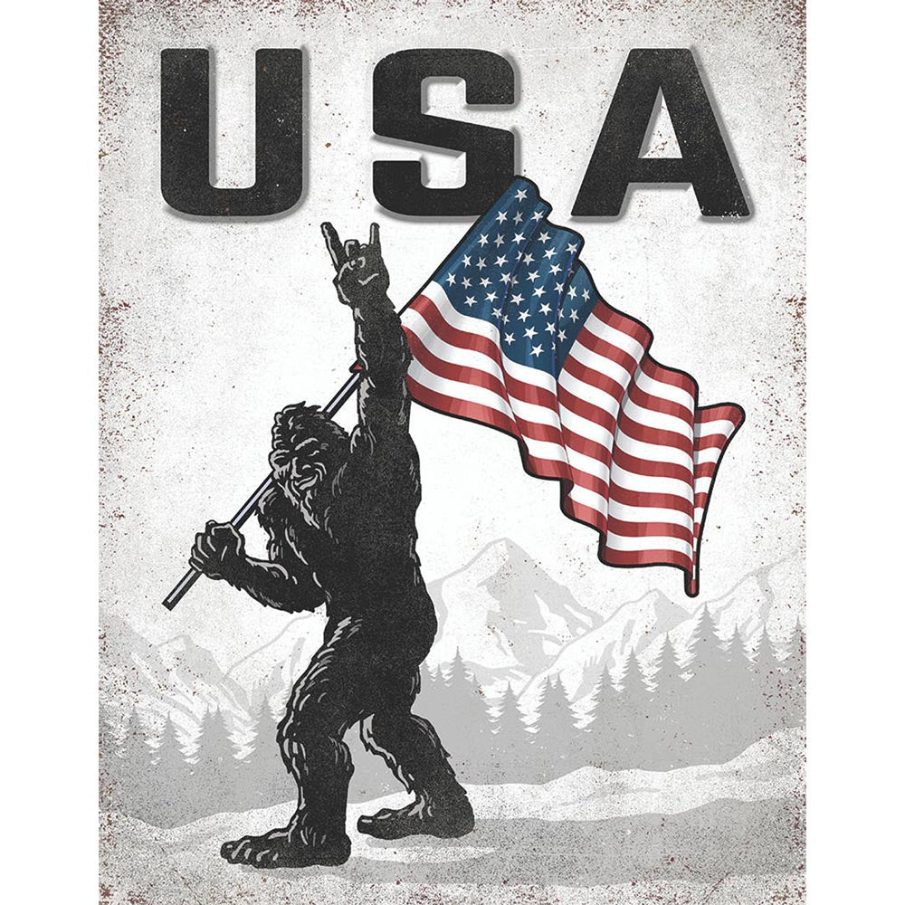 Bigfoot illustration holding a waving American flag with "USA" in bold text above, set against a mountain backdrop.